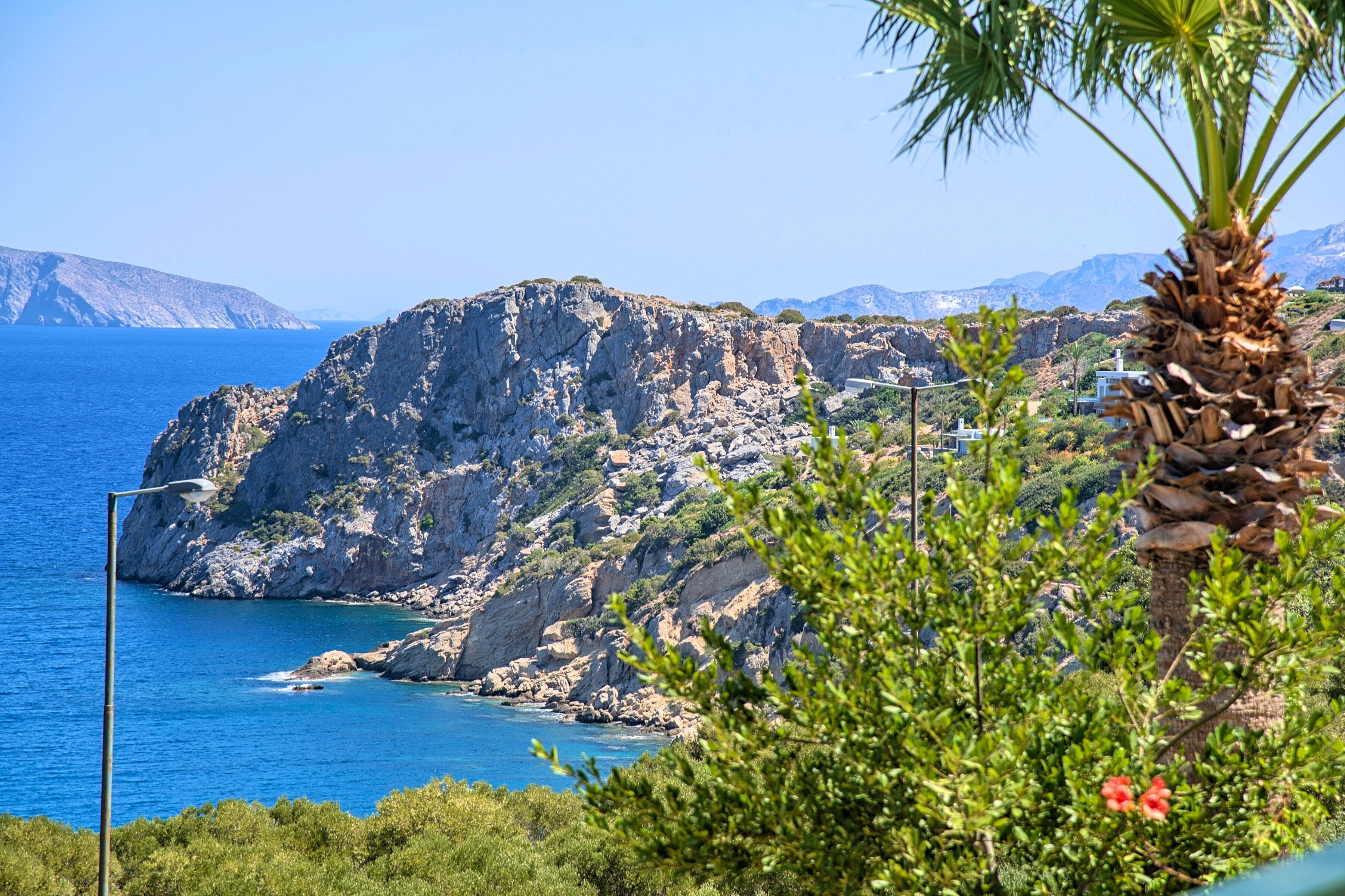 A coastal landscape with rocky cliffs, a clear blue sea, and lush greenery.