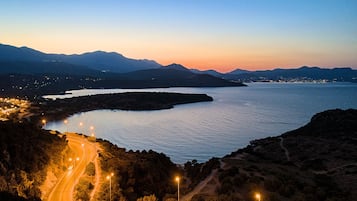 A coastal road winding through a mountainous landscape with a body of water and distant city lights.