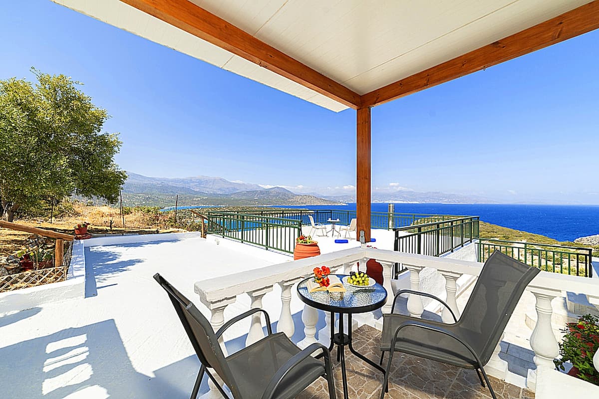 A terrace with a table and chairs, overlooking a scenic view of the sea and mountains.