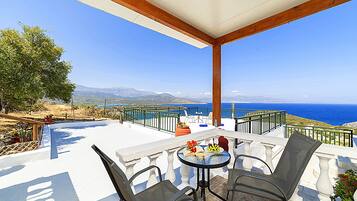 A terrace with a table and chairs, overlooking a scenic view of the sea and mountains.