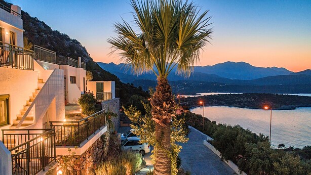 A modern building with a staircase, a palm tree, and a view of mountains and water. - Istron Homes (Agios Nikolaos)