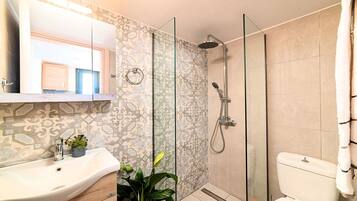 A bathroom with a glass shower enclosure, a sink with a mirror above it, and a toilet.