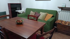 A living room with a green sofa, wooden dining table, and a bowl of food.