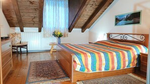 A bedroom with a wooden bed, a chair, a desk, a radiator, and a window with curtains.