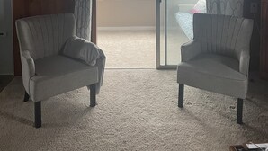 A room with wooden ceiling, two armchairs, a carpeted floor, a sliding glass door, and a framed picture on the wall. - Cozy Little Blue Cottage by the Bay (Milford)