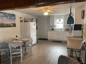 A compact kitchen with white cabinets, a refrigerator, a microwave, and a dining area with a table and chairs.