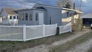 A single-story house with a white picket fence, a garage, and a small porch. - Cozy Little Blue Cottage by the Bay (Milford)