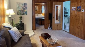 A cozy room with wooden walls, a bed, a sitting area with a couch and a coffee table, and a bathroom visible through an open door. - Cozy Little Blue Cottage by the Bay (Milford)
