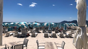 Een zitgedeelte aan het strand met parasols en ligstoelen, met uitzicht op zee.