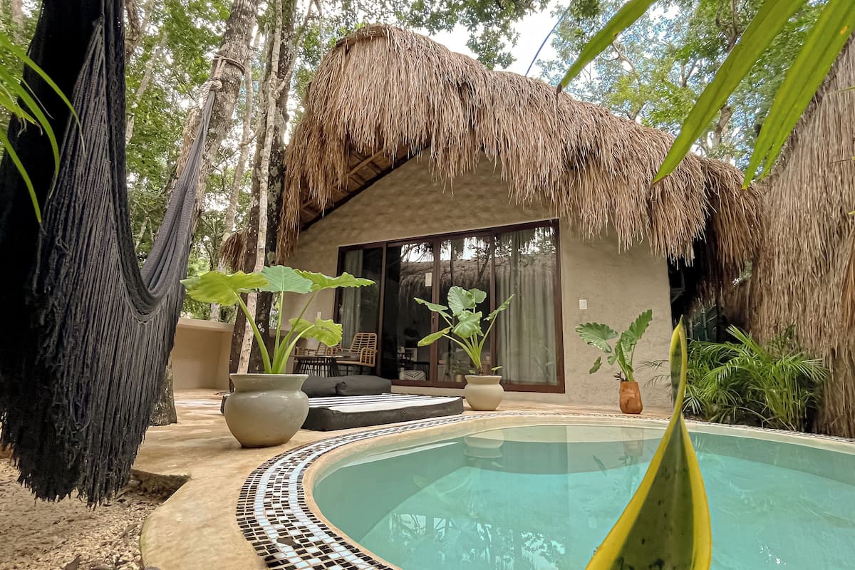 A poolside area with a thatched-roof structure, outdoor seating, and tropical plants.