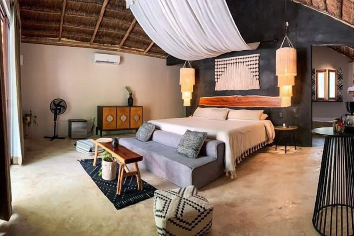 A bedroom with a bed, bedside tables, a hanging light fixture, a fan, and a small round table.