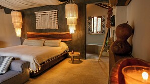 A cozy bedroom with a large bed, two hanging lamps, a small round table, and a wooden sculpture.