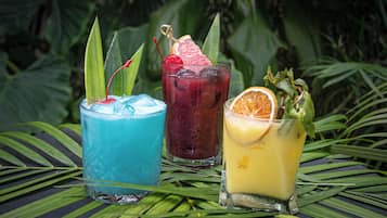 Tres bebidas coloridas sobre una mesa con hojas tropicales.
