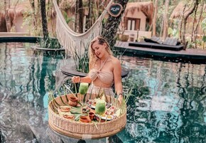 Une femme se tient près d’une piscine, un panier rempli de nourriture et de boissons à ses côtés.