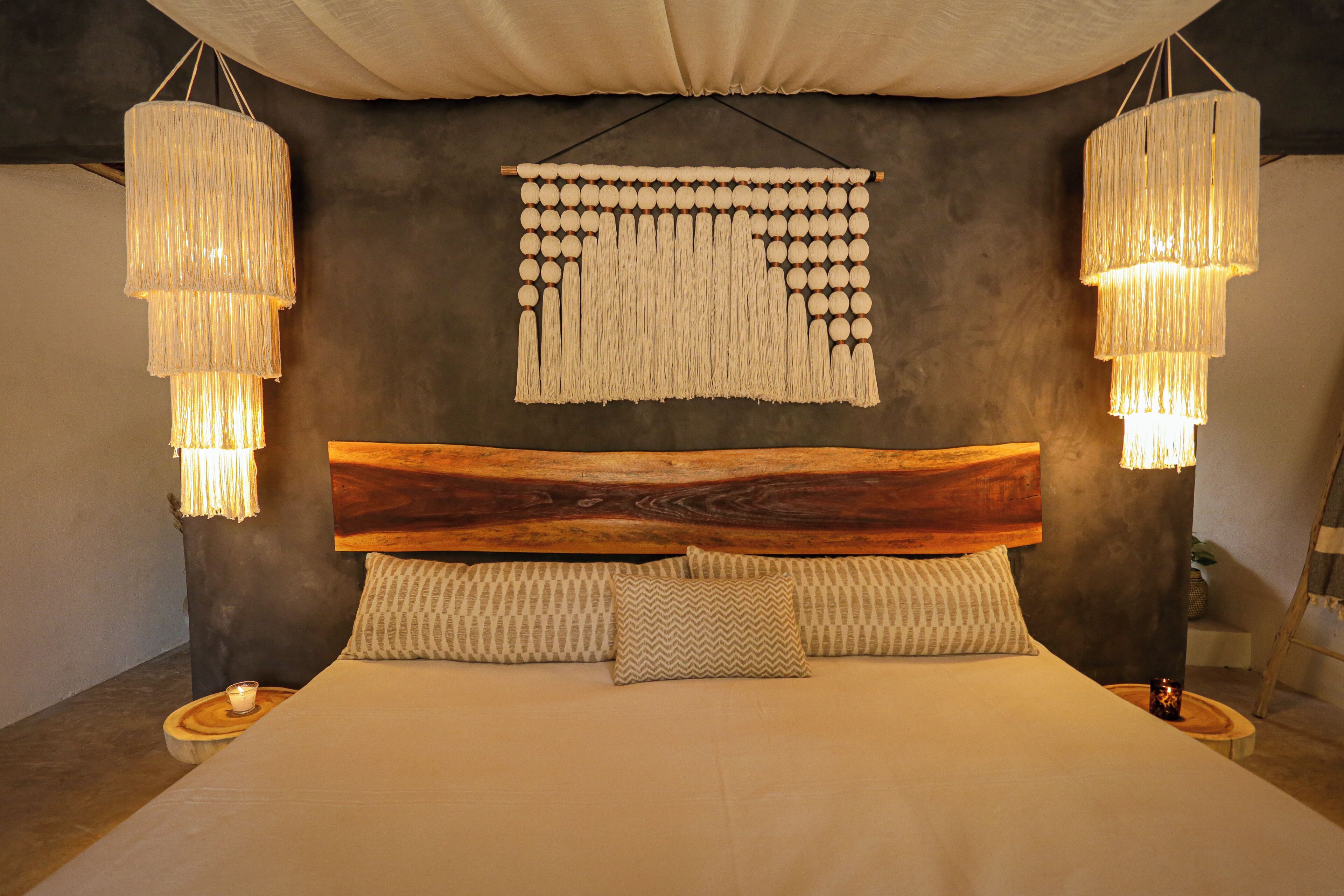 Une chambre avec une tête de lit en bois, une décoration murale en macramé et deux lampes suspendues.