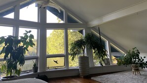 Ein Zimmer mit großen Fenstern, einer geneigten Decke und einigen Blumentöpfen.
