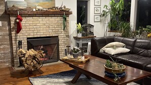Ein gemütliches Wohnzimmer mit Kamin, einem Couchtisch mit Pflanzen, einer Ledersofa und einem blauen Teppich mit Muster.