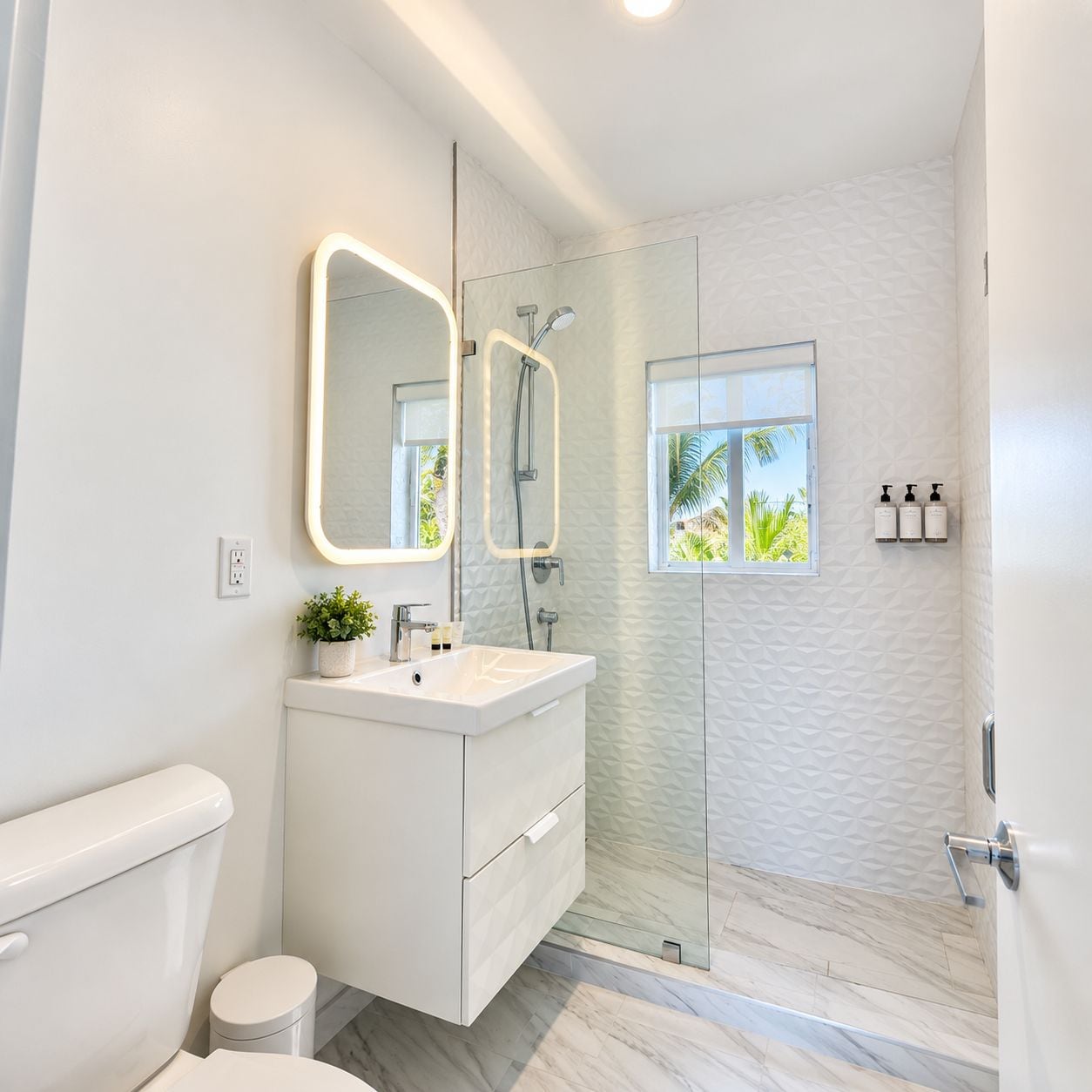 Un bagno moderno con box doccia in vetro, un mobile lavabo bianco con specchio e una finestra che offre luce naturale.