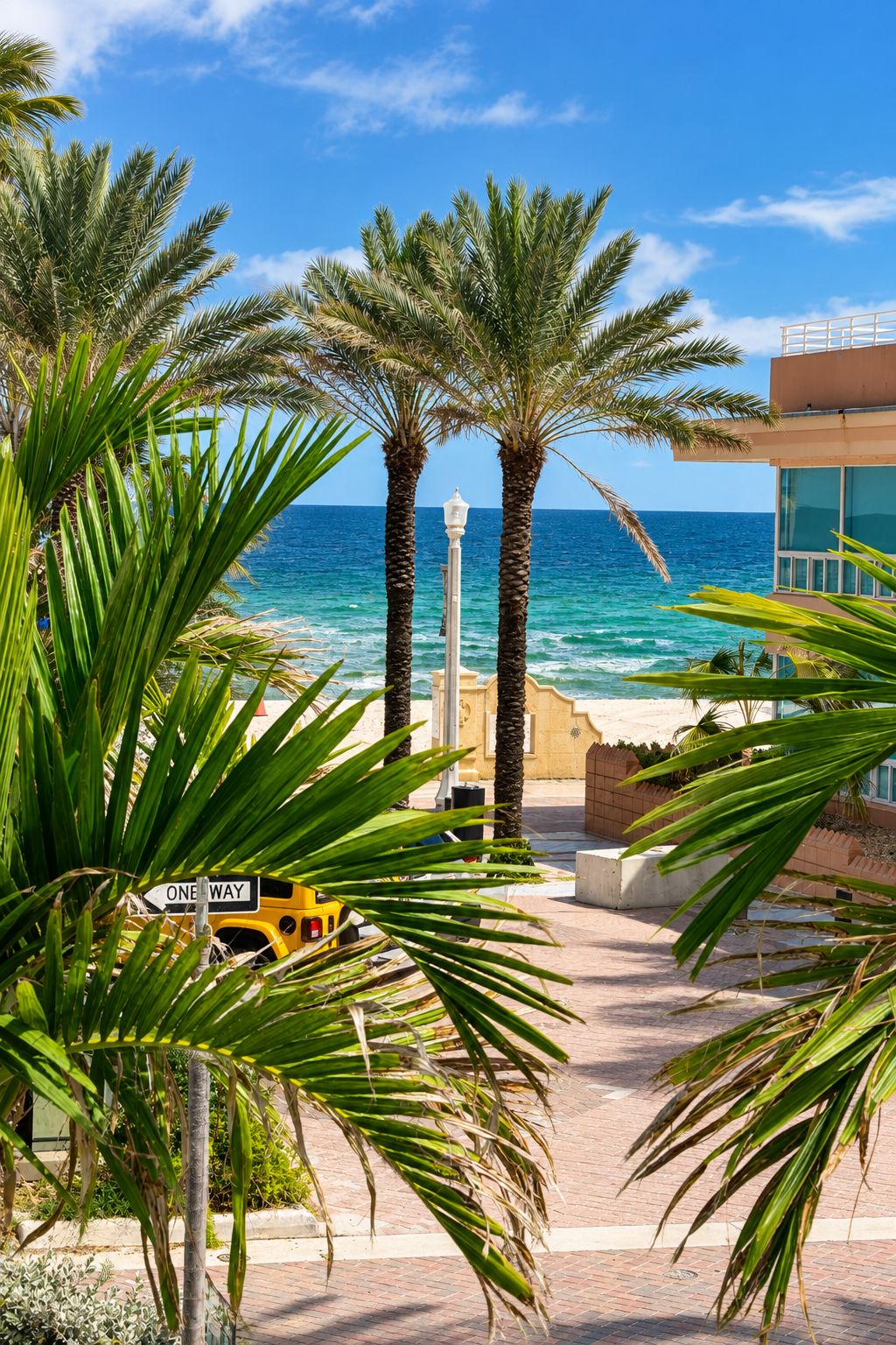 A pathway leading to a beach with palm trees, a one-way sign, and a building with a view of the ocean.
