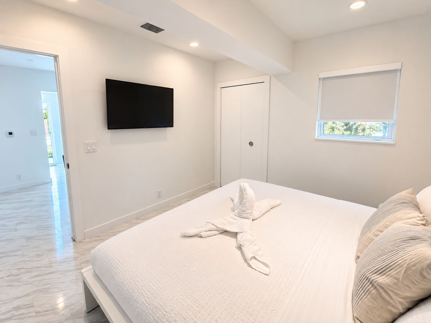 A modern bedroom with a bed, a flat-screen TV, a wardrobe, and a window.