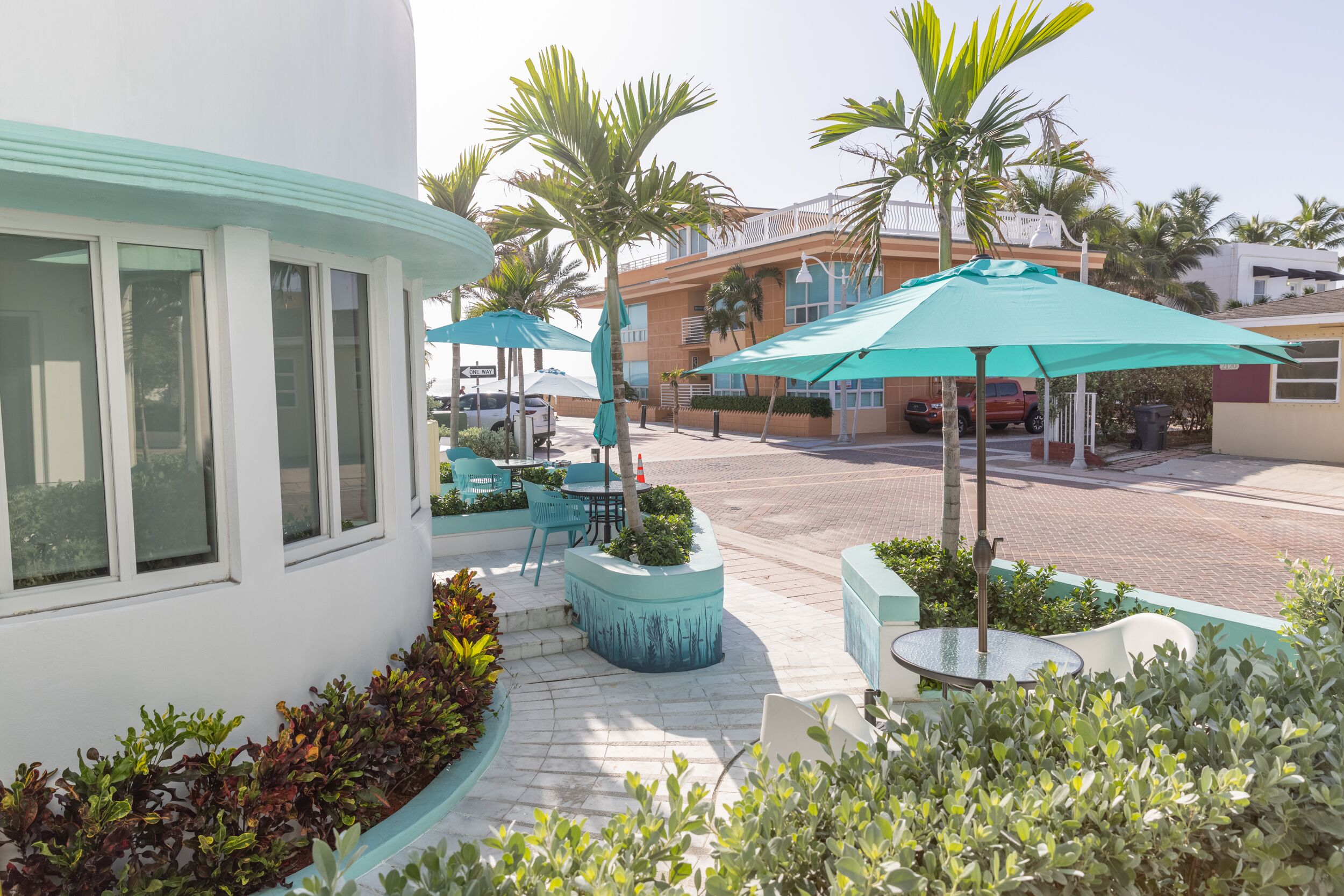 A patio area with outdoor seating, palm trees, and a building with large windows.