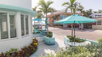 A patio area with outdoor seating, palm trees, and a building with large windows.