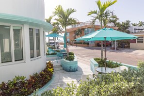 Un patio con mobiliario exterior, palmeras y un edificio con amplios ventanales.