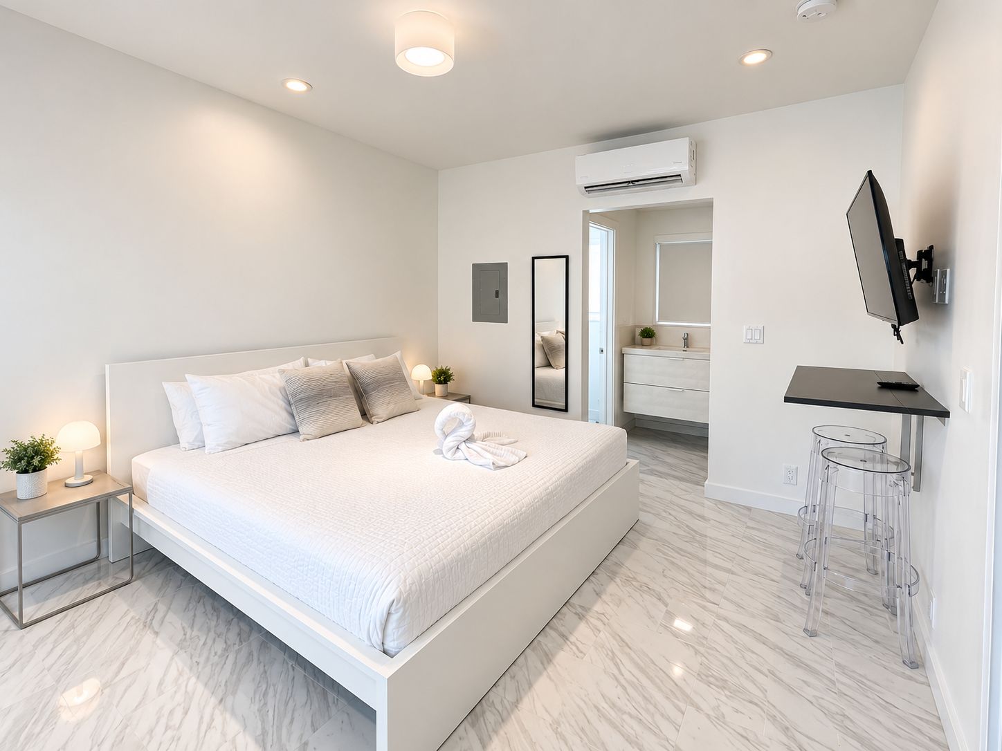 A modern hotel room with a large bed, bedside lamps, a flat-screen TV, and a bathroom with a mirror and sink.