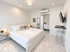 A modern hotel room with a large bed, bedside lamps, a flat-screen TV, and a bathroom with a mirror and sink. - The Marlin Beachside (Hollywood)