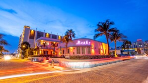 A hotel with a neon sign, palm trees, and a paved walkway.