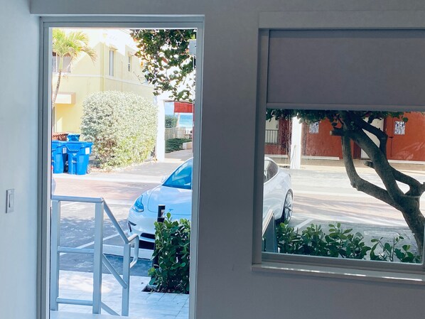 A view through a window of a street with parked cars, a tree, and a building with a red wall. - The Marlin Beachside (Hollywood)