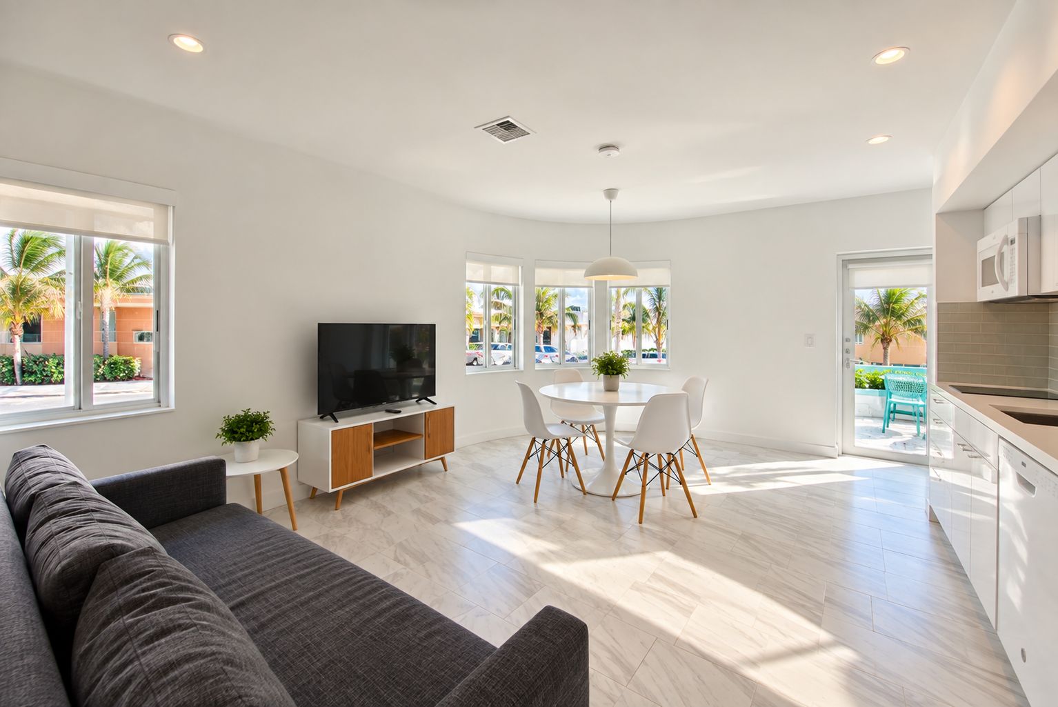 A modern living room with a flat-screen TV, a sofa, a dining table with chairs, and a kitchen area with cabinets.