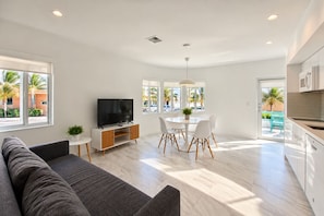 A modern living room with a flat-screen TV, a sofa, a dining table with chairs, and a kitchen area with cabinets. - The Marlin Beachside (Hollywood)