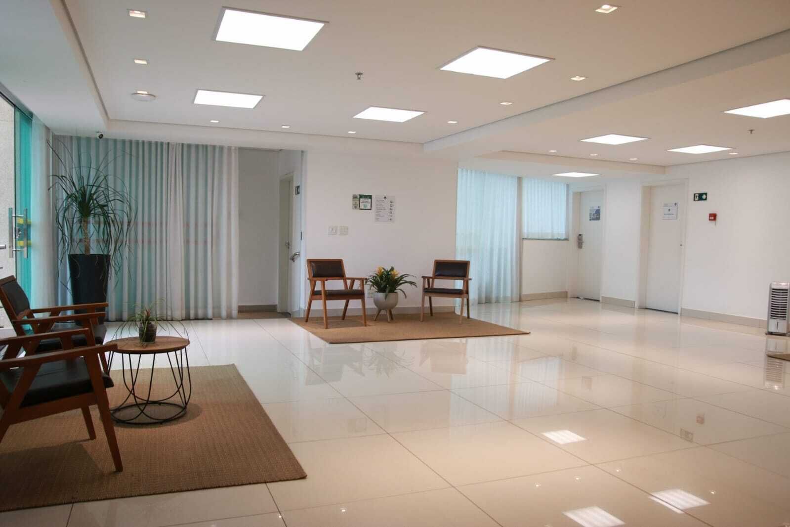 Um lobby amplo com design moderno e elegante, apresentando uma área de recepção com balcão e cadeiras, uma grande planta em vaso e piso revestido com azulejos.