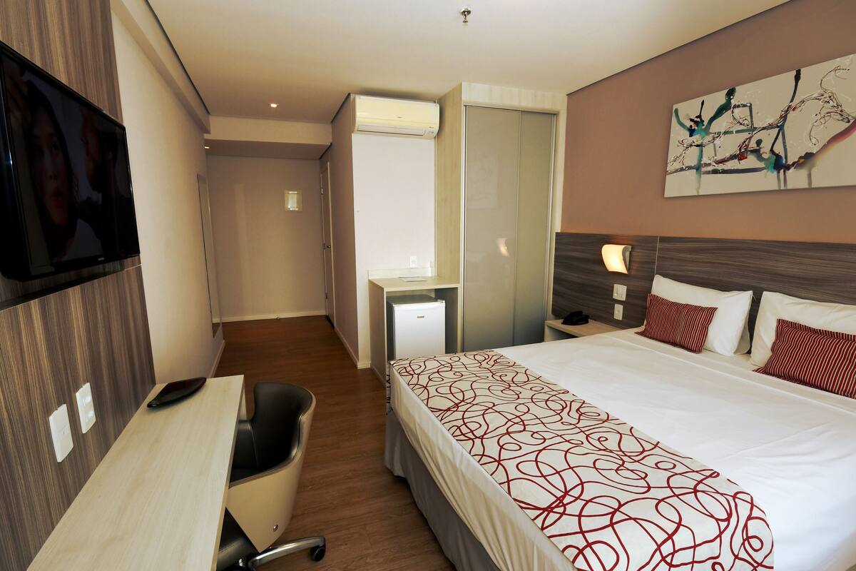 Habitación de hotel con cama, escritorio, silla, televisor y una pequeña kitchenette.