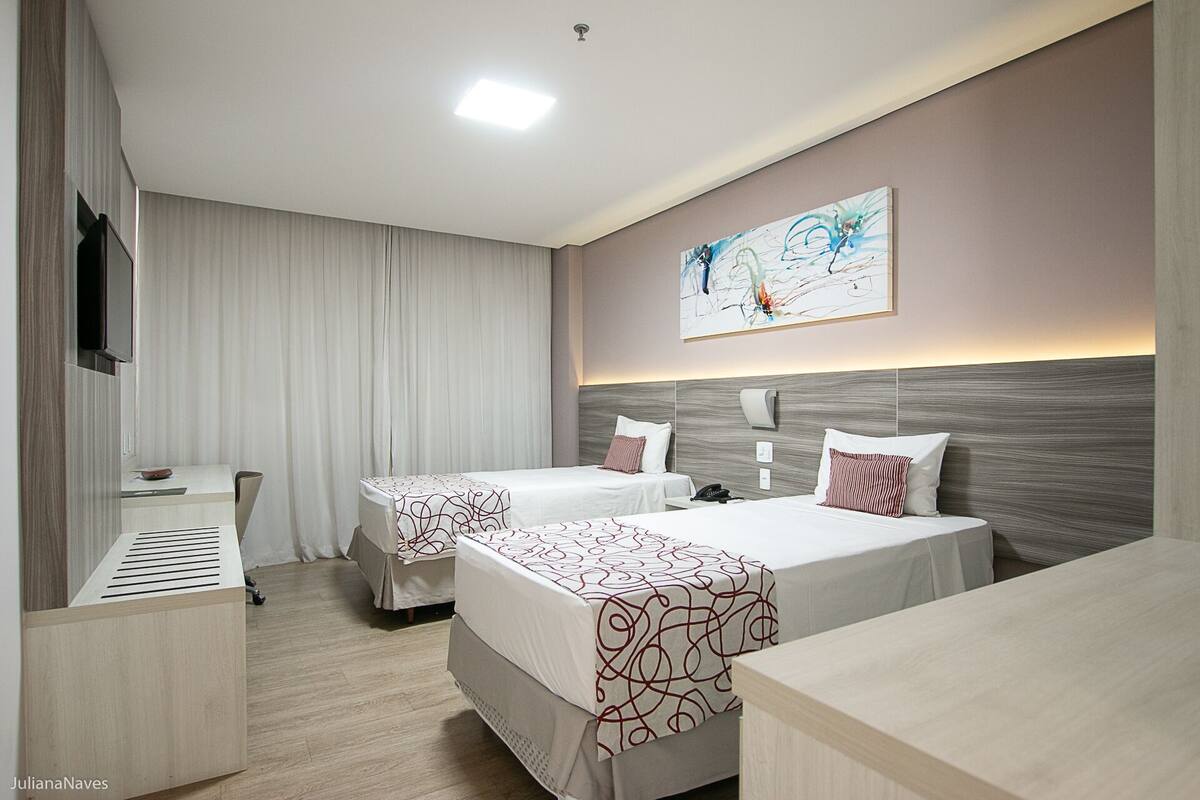 Habitación de hotel con dos camas, un escritorio, un televisor y un cuadro en la pared.