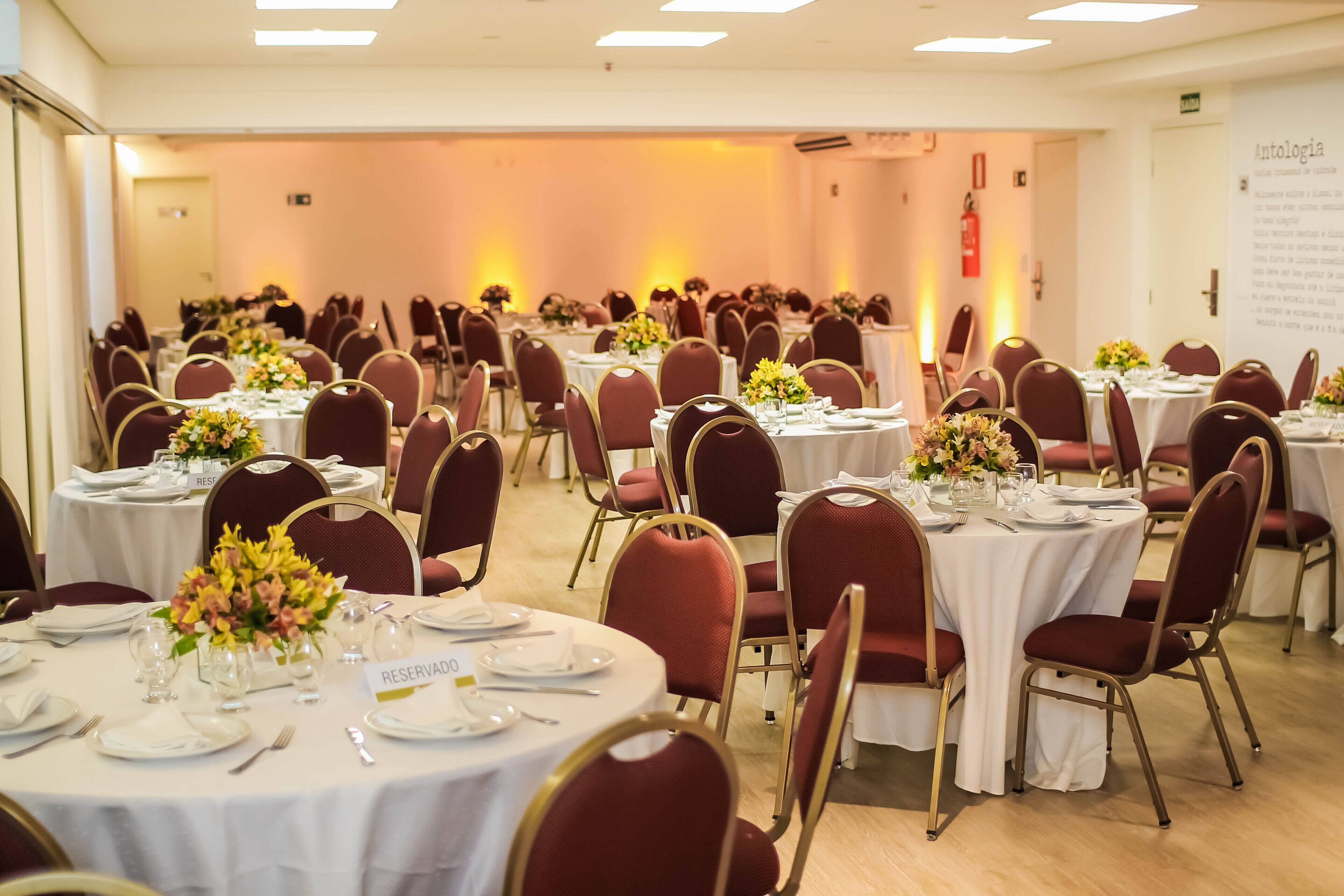 A banquet hall with round tables set for dining, each with white tablecloths and red chairs.