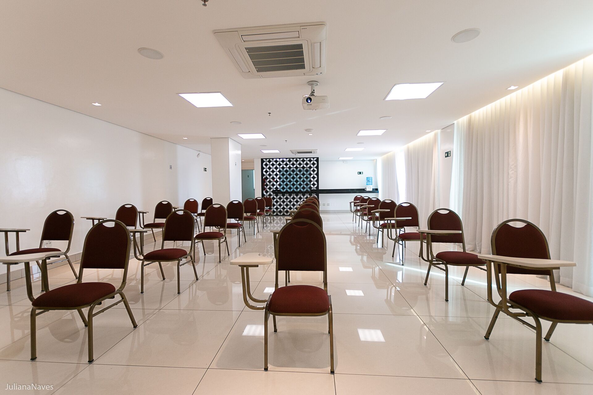 A conference room with rows of chairs and tables, white walls, and a patterned wall divider.