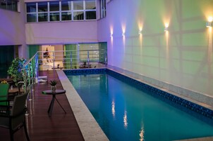 Piscina interna com deck de madeira, área de estar e vista do espaço interno.