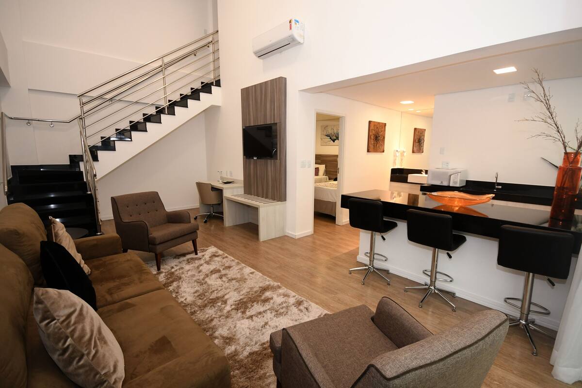 Una sala de estar moderna con una escalera, una zona de cocina con taburetes de bar y un comedor.