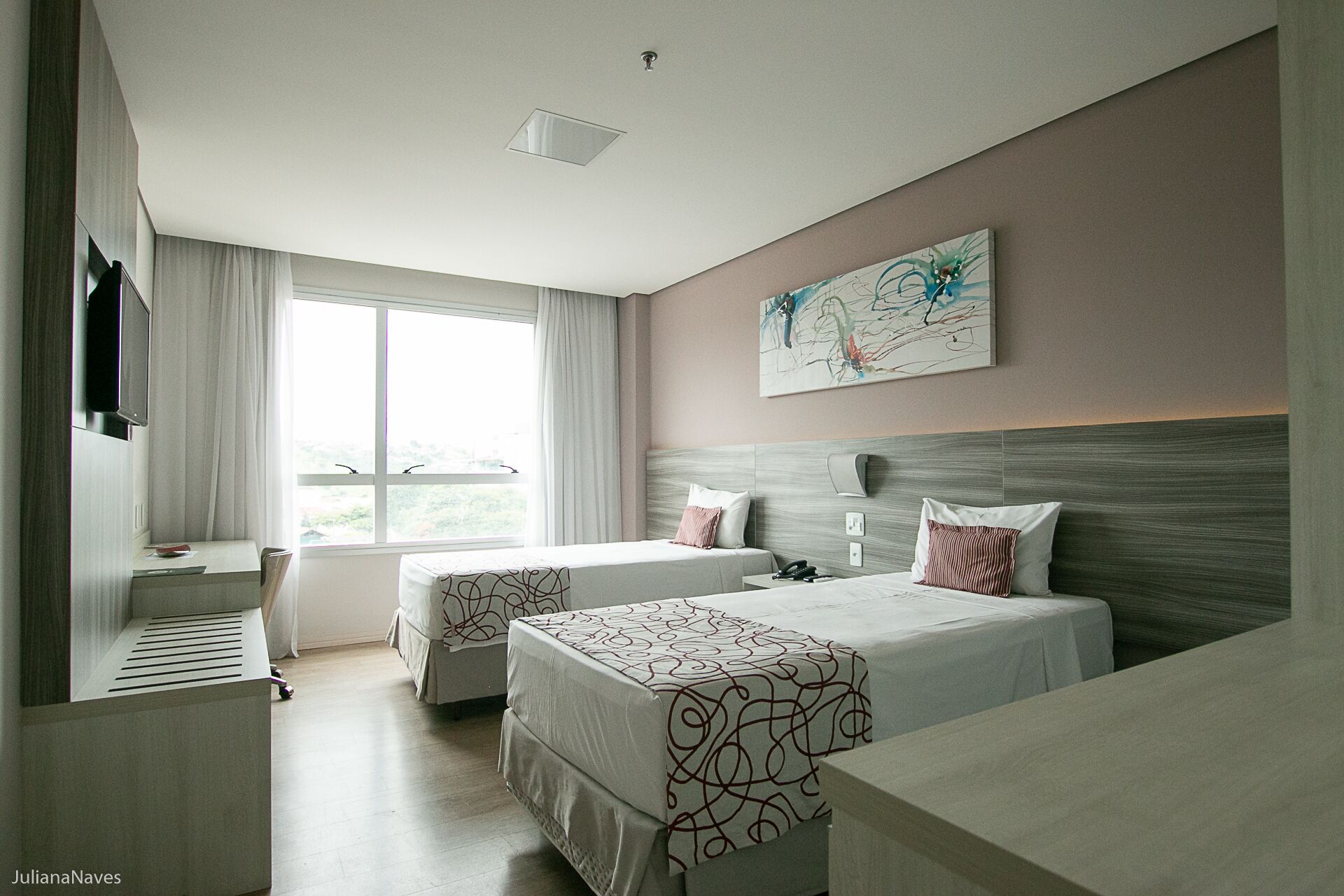 A hotel room with two beds, a desk, a TV, and a large window.
