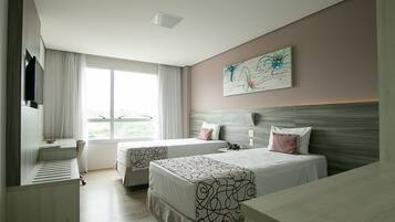 A hotel room with two beds, a desk, a TV, and a large window.