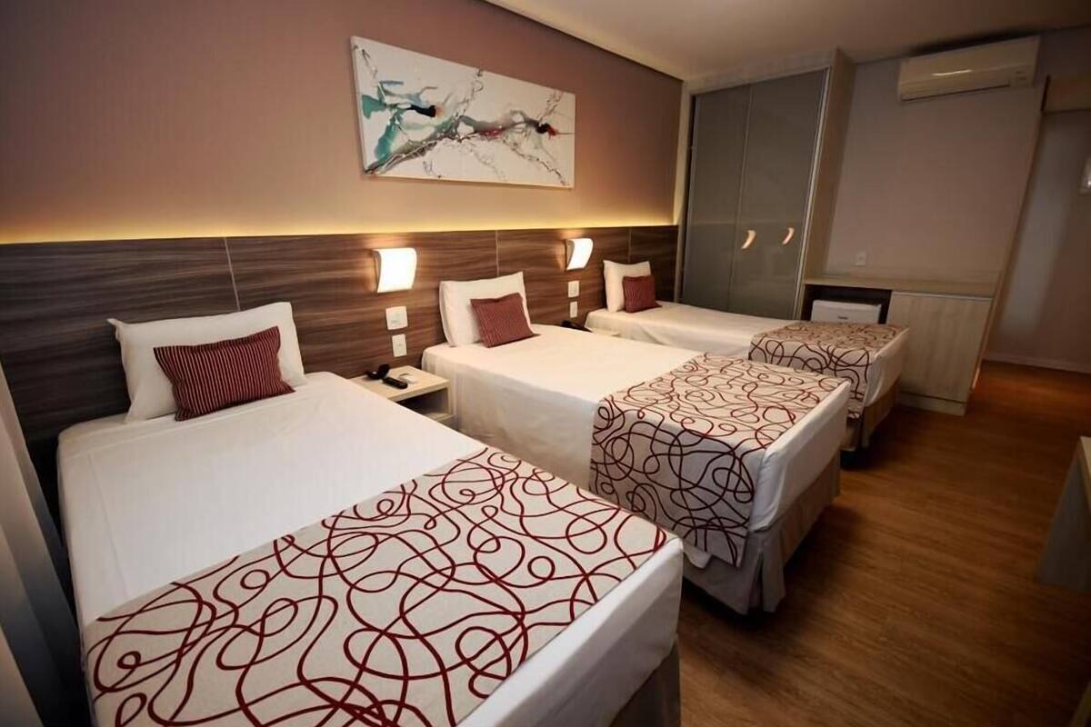 Habitación de hotel con tres camas, cada una con una colcha estampada, un cuadro abstracto grande en la pared y un armario empotrado.