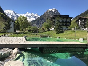 Eine Holzterrasse über einem klaren Pool, mit einem Berg im Hintergrund.