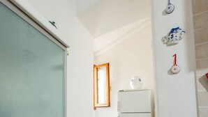 Un couloir étroit avec un réfrigérateur blanc, un plancher en bois et une porte en verre dépoli.