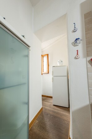 A narrow hallway with a white refrigerator, a wooden floor, and a frosted glass door.