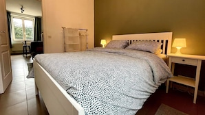 A bedroom with a bed, two bedside tables with lamps, a chair, and a window with curtains. - L'appartement d'Houyet (Houyet)