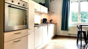 A modern kitchen with white cabinets, a built-in oven, a coffee maker, and a window with a view of greenery. - L'appartement d'Houyet (Houyet)