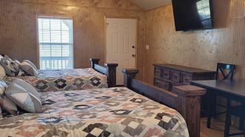 A room with two beds, a wooden dresser, a table, and a TV mounted on the wall.