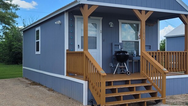 A small, single-story building with a porch and a grill. - Cozy New Cabins (Seadrift)